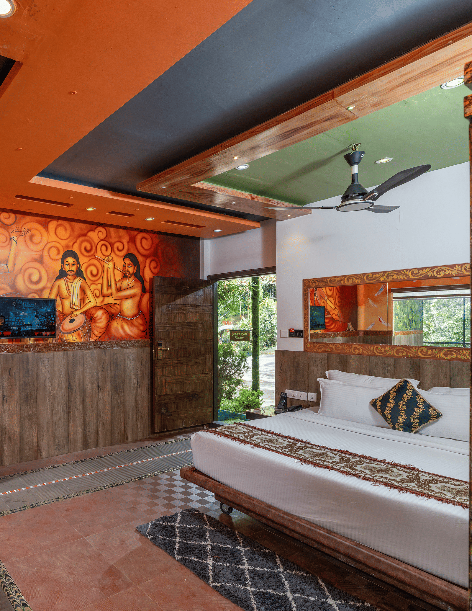The interior of the Jungle Room at Parakkat Nature Hotel and Resorts, Munnar, featuring a large bed, artistic wall murals, reflective ceiling panels, and floor tiling.