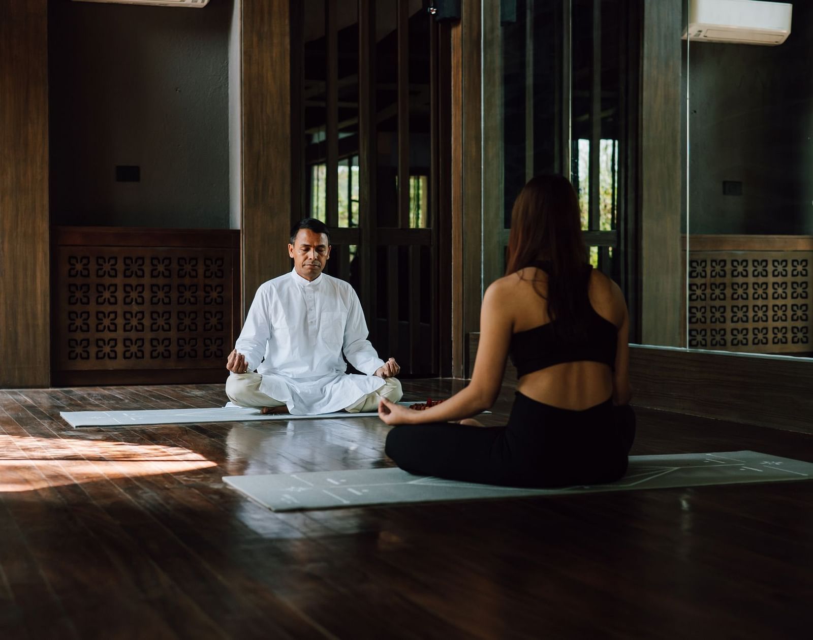 A man in white attire teaching a woman meditation indoors.