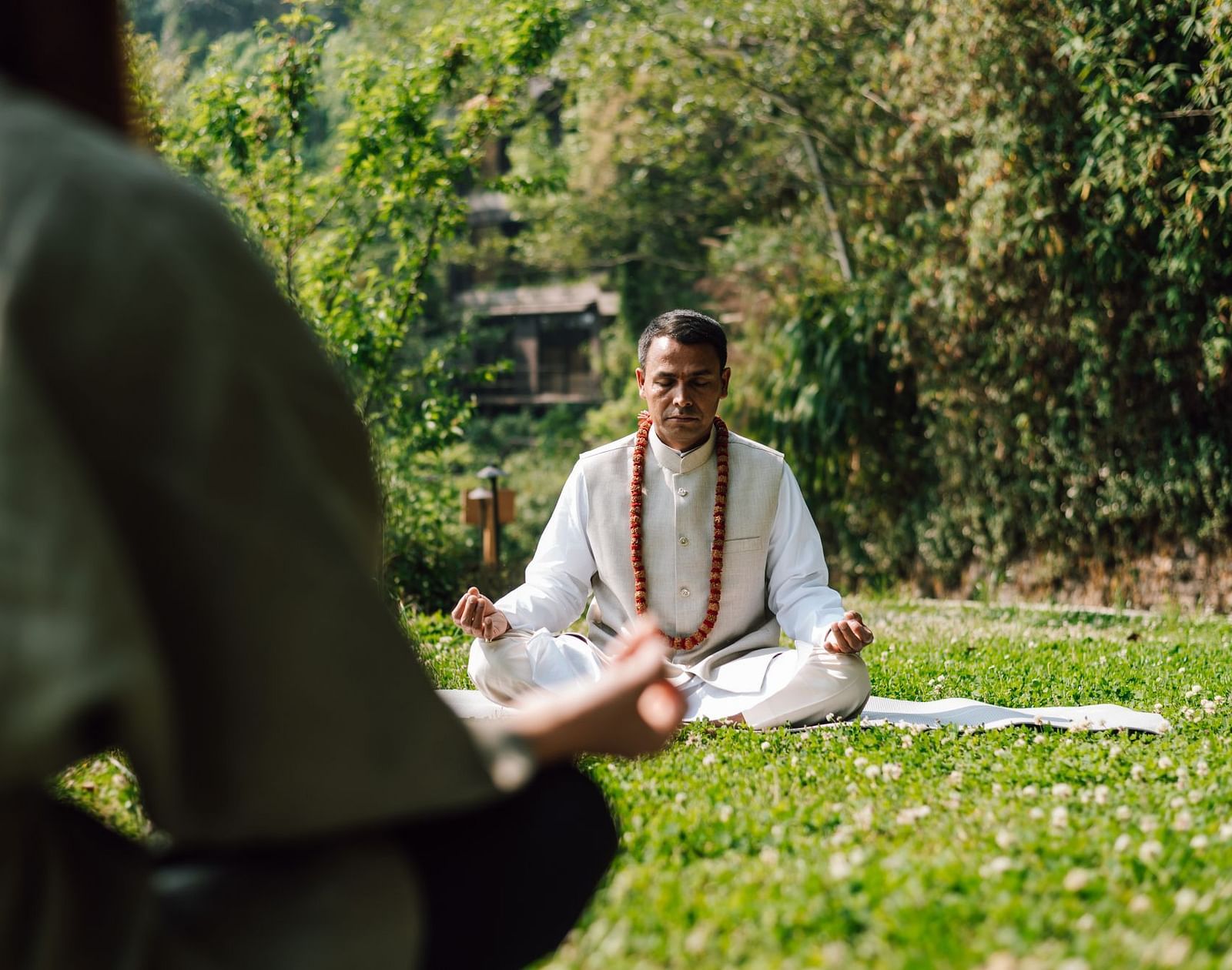 Person meditating outdoors in a peaceful garden setting, surrounded by greenery.