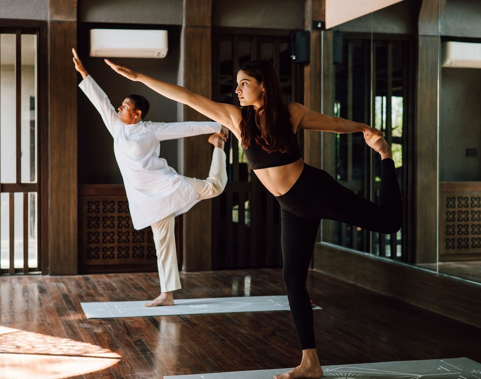 Two individuals practicing yoga indoors, performing balance poses with focused expressions.