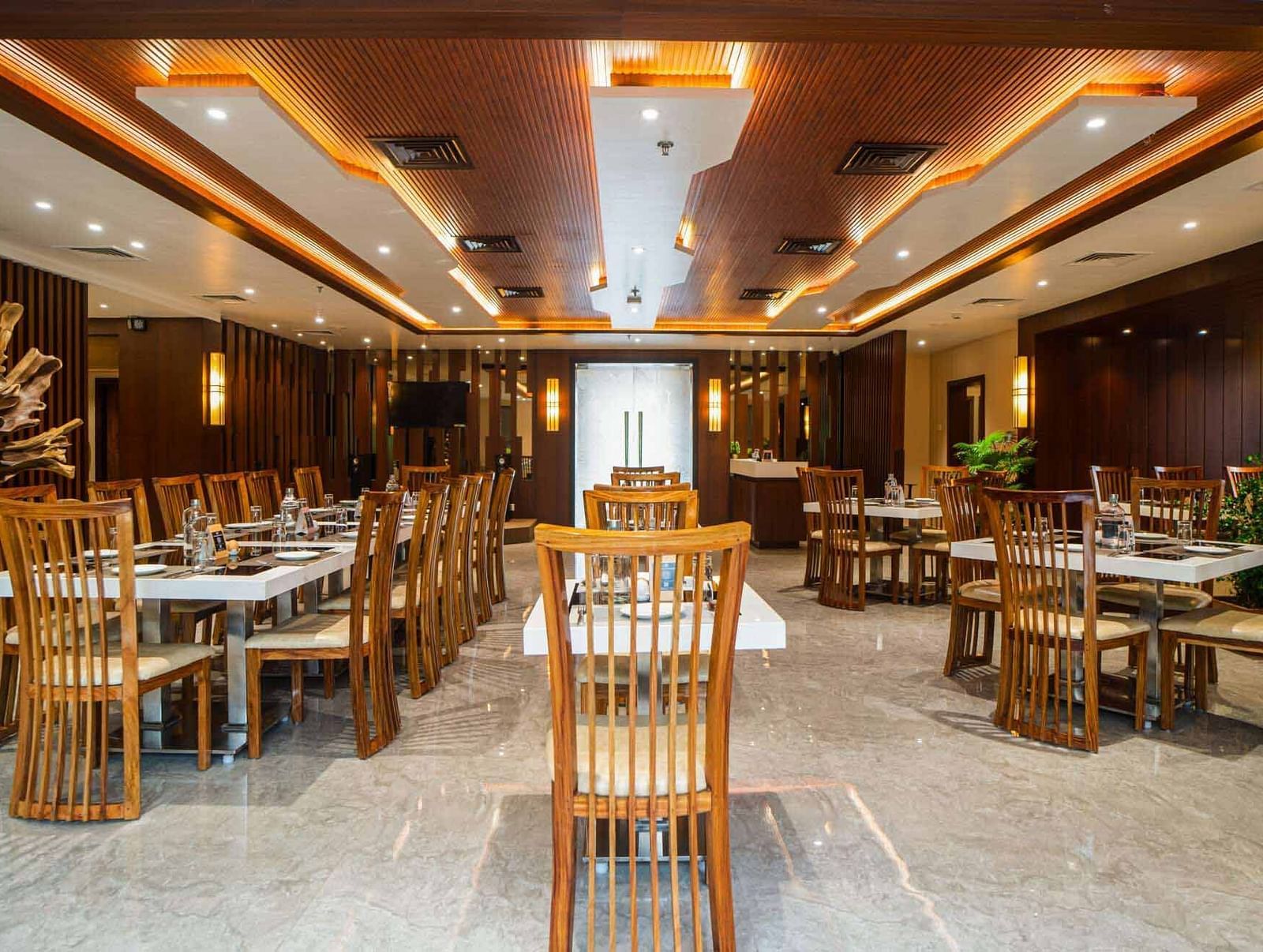 The spacious dining hall at Mansha Palace is furnished with numerous set tables and comfortable wooden seating.