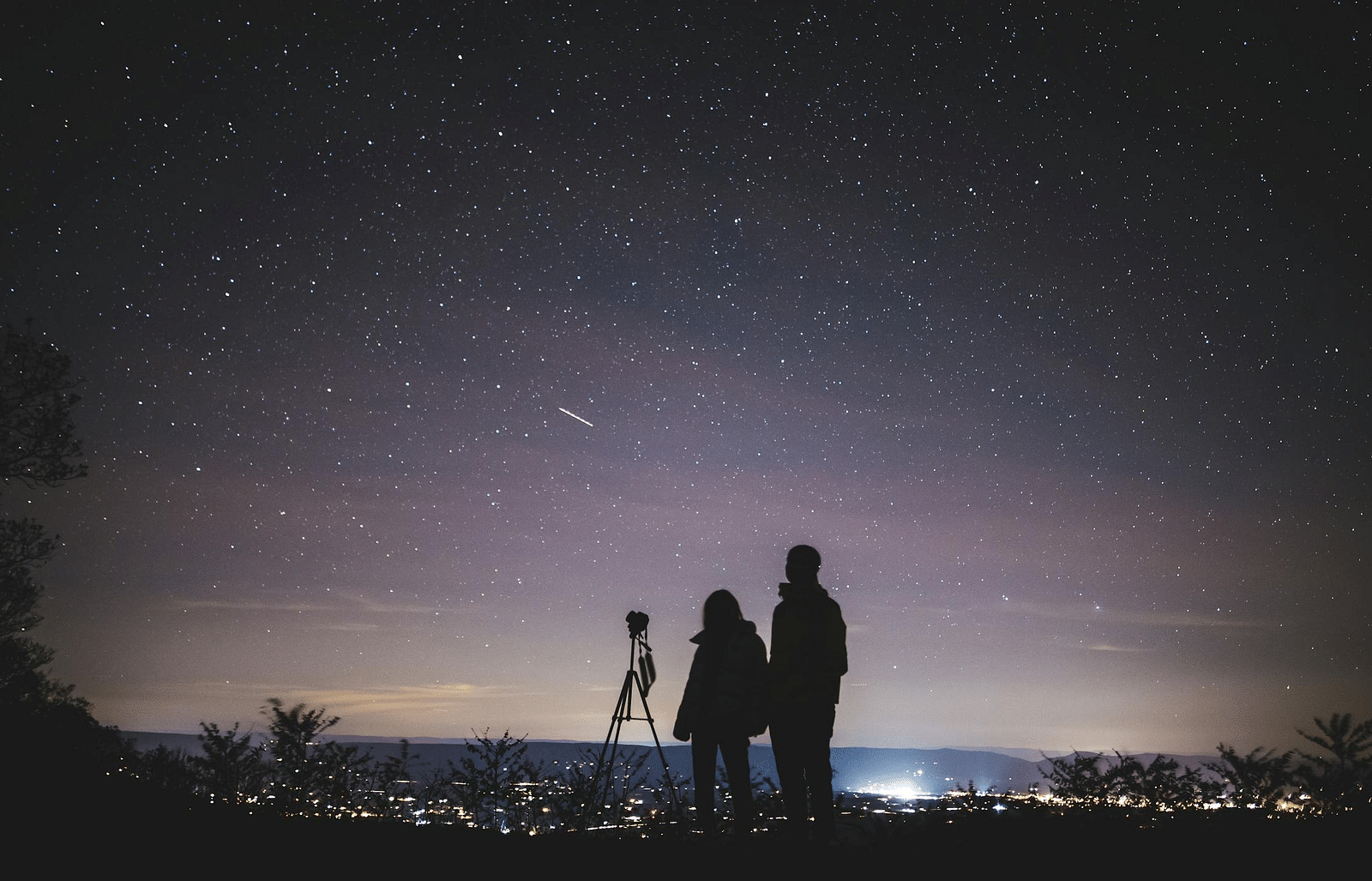 An image of a couple staring at a sky during the night with full of stars 