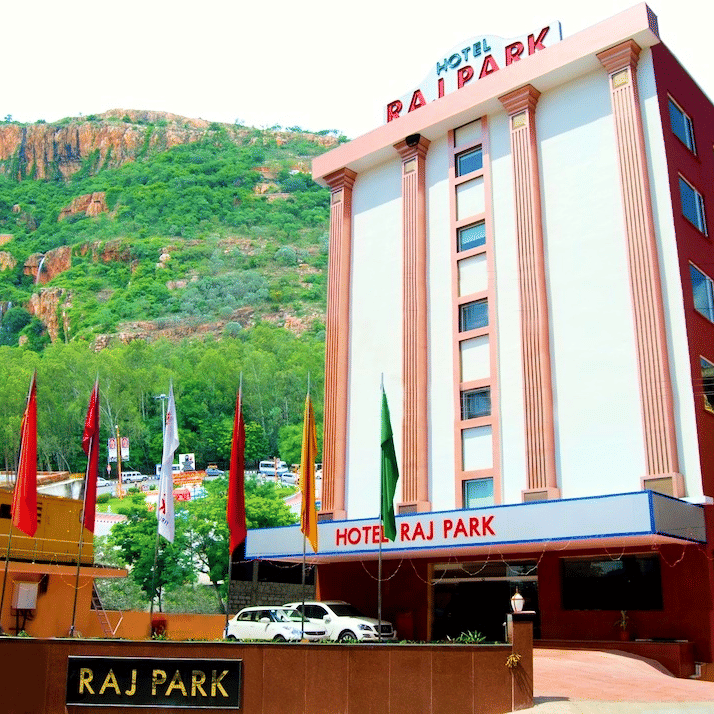 Facade of Raj Park Hotel, Tirupati, with a green mountain in the background.