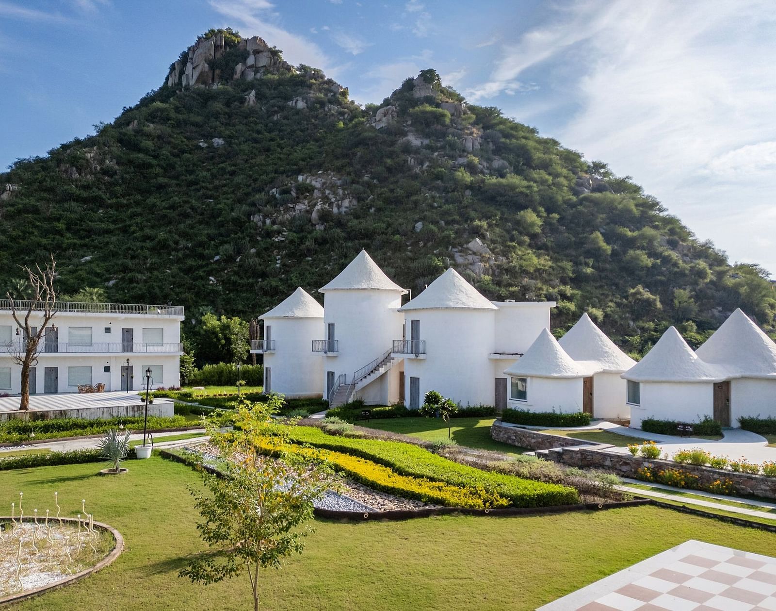 Conical-roof accommodations with an open space in front, set against a scenic mountain backdrop at Valley by Grassfield.