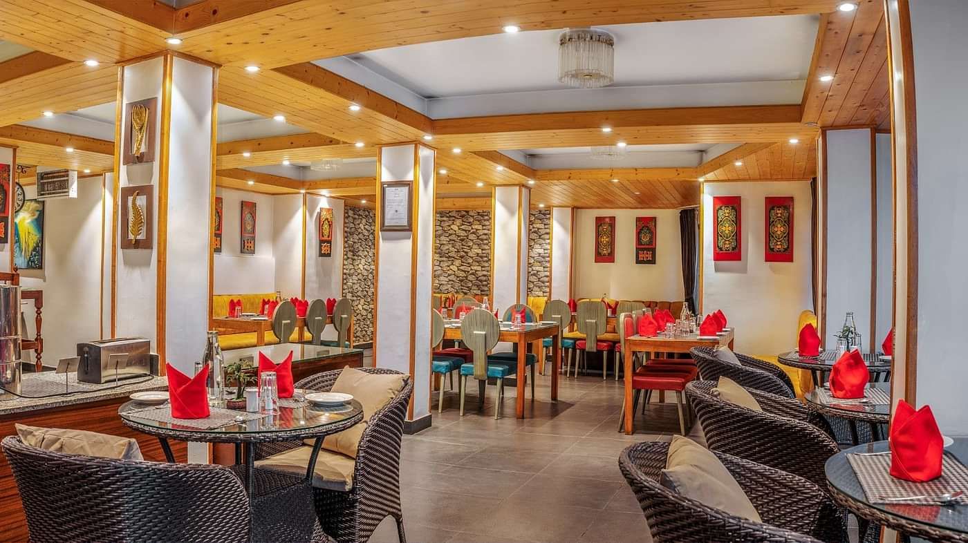 Modern restaurant interior with neatly arranged tables and chairs, red napkins on tables, warm lighting, and decorative wall art at Summit Swiss Heritage Resort & Spa, Mall Road