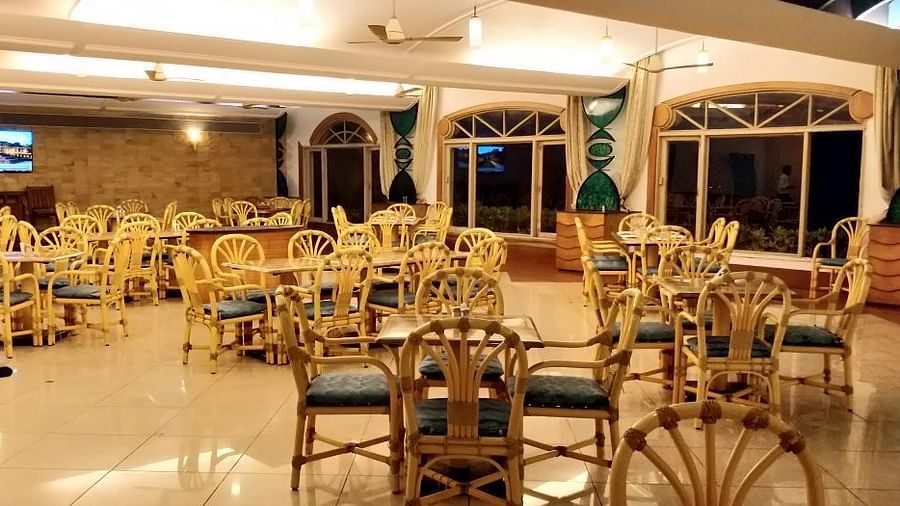 A brightly lit Flavors Restaurant dining area with numerous golden-framed chairs and tables, and large windows looking outdoors at Kohinoor Samudra Beach Resort, Ratnagiri