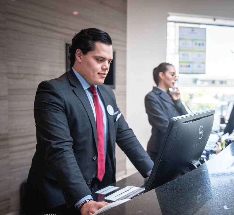 2 staff members standing behind the reception desk looking at the computer in front of them.