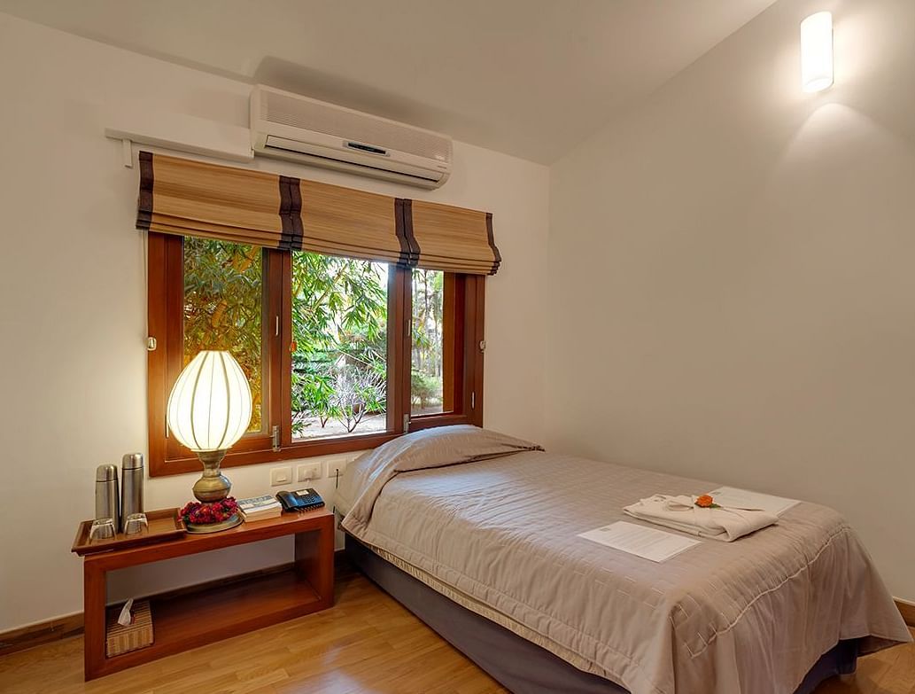 A bedroom with a low bed, a window with blinds, and a lamp - Shreyas Retreat