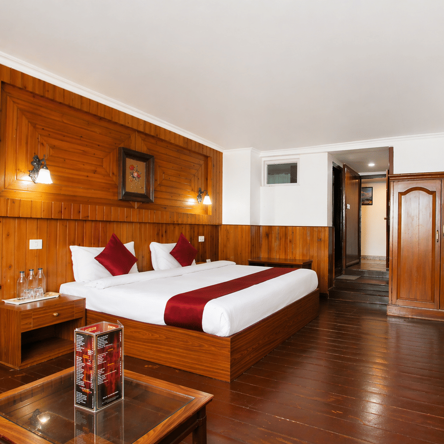 A room at Central Hotels featuring a king bed with red and white bedding rich wooden wall panels a wall-mounted TV wooden door dark hardwood flooring and a coffee table.