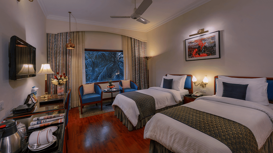 A Premiere Room at The Clarks Varanasi featuring twin beds, a ceiling fan, a wall-mounted television, and a seating area at The Clarks Varanasi.