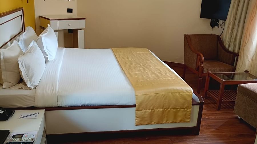 A room at Ras by Treat Resorts, featuring a neatly made bed, a telephone on the side table, a coffee table, a wooden chair, and a TV.