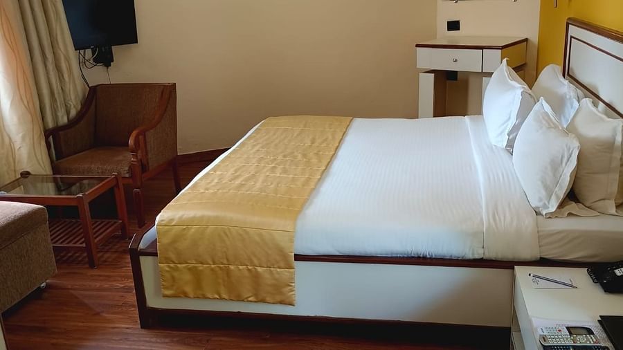 A room featuring a neatly made bed, a telephone placed on a side table, a coffee table, a wooden chair, and a TV - Ras by Treat Resorts
