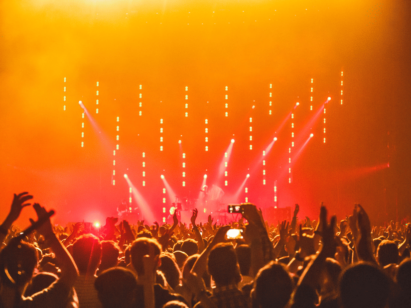 Audience cheering and capturing moments as performers take the stage beneath dramatic orange lighting