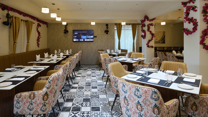 An indoor restaurant dining area with multiple set tables, patterned chairs, a TV screen, and floral garland decorations | Voyage Eastin Suites