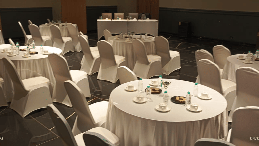 The elegant banquet space at Vinti Resort, Ambaji is set with round tables, white linen, and covered chairs for a special dinner event.