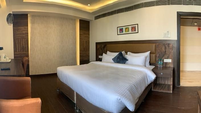 A close-up of a neatly made bed in a hotel room, with a partially visible sofa - VITS Gurugram