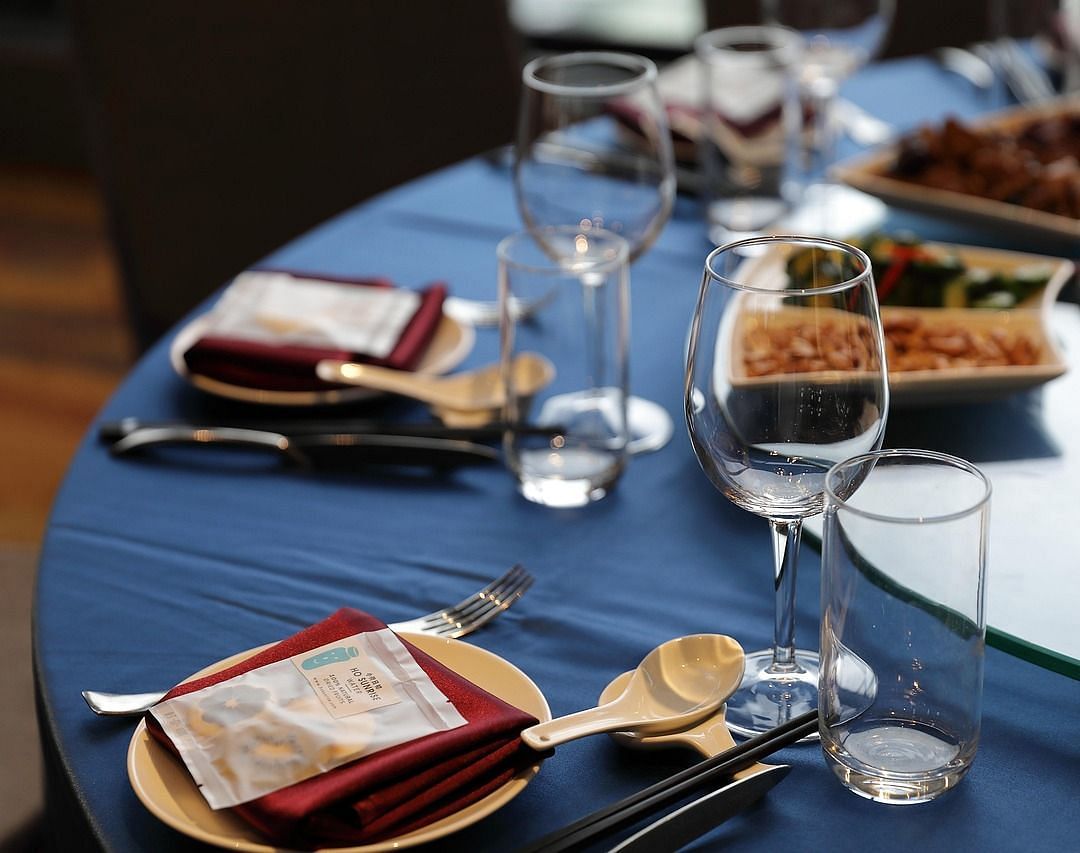 A close up shot of a round dining table with sparkly glassware and cutlery arranged on it.