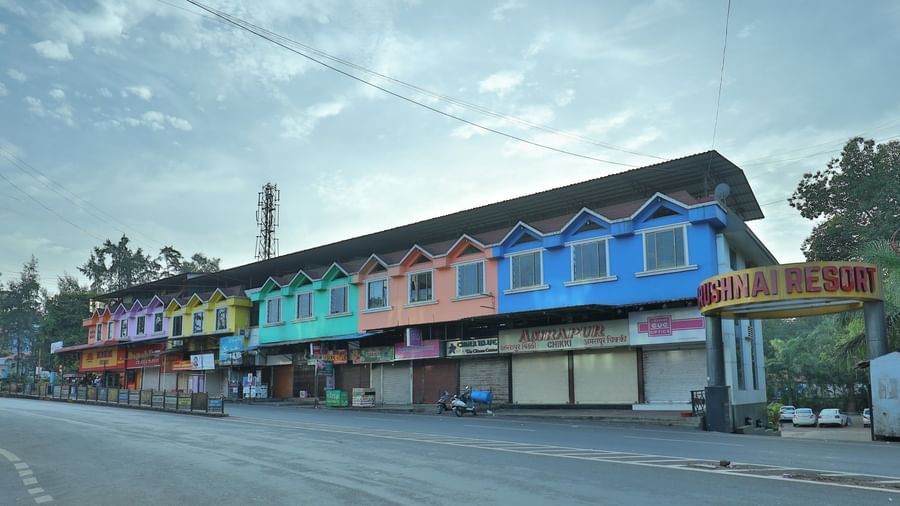 The Krushnai Resort sign marks a long building with colourful facade lining a quiet road under a cloudy sky.