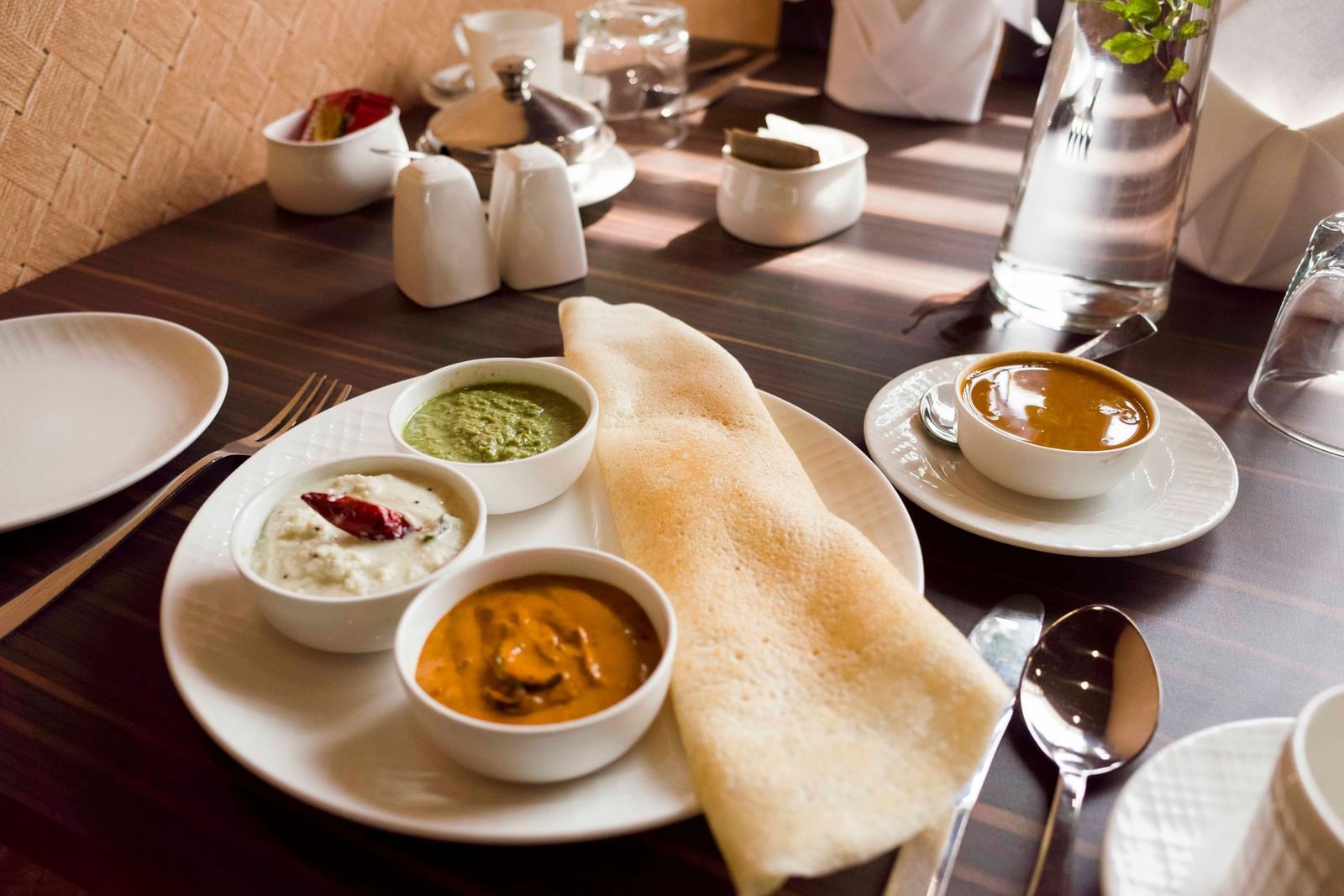 A South Indian meal with dosa and various chutneys served on a plate | Daksh The Madhuvan Suites
