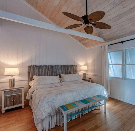 Bright bedroom with a double bed, ceiling fan, white walls, and a baby crib placed near the window in a guesthouse | Abaco Inn