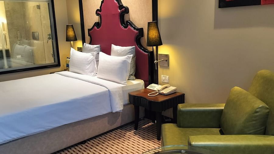 Elegant hotel room with plush bed, padded headboard, and a sitting area with a small table.