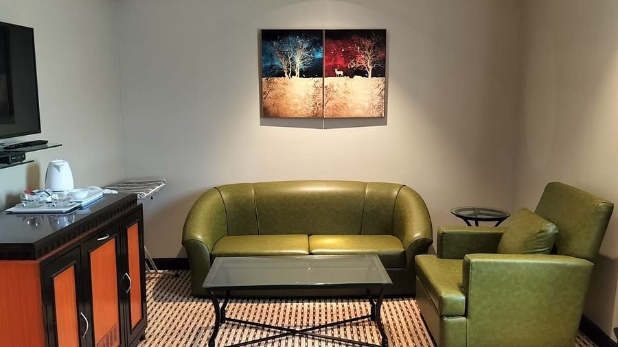 Cosy hotel room corner with a single bed, wall-mounted TV, armchair, and writing desk.