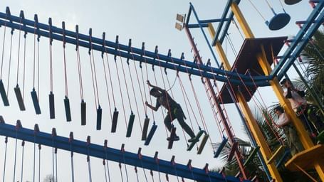 Silhouetted figures climb an outdoor adventure course structure with ropes and ladders