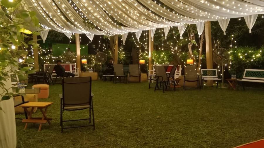 An illuminated outdoor event space at dusk, showing a large lawn area with tables, chairs, and overhead lighting | Vedic Village Spa Resort, Kolkata
