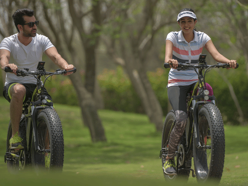 A couple riding bicycles with trees in the background - Karma Lakelands.