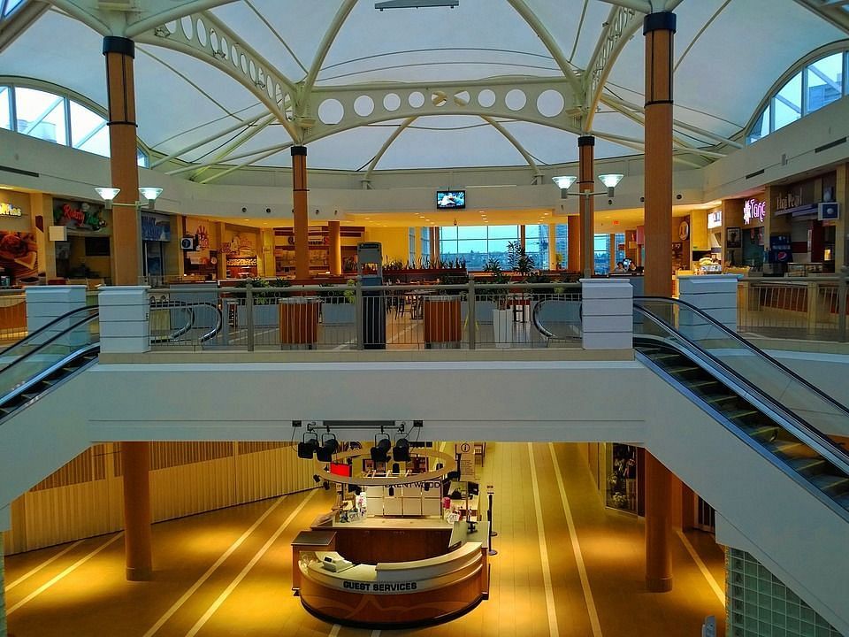 A large, multi-level shopping mall with escalators, a food court, and various retail stores.