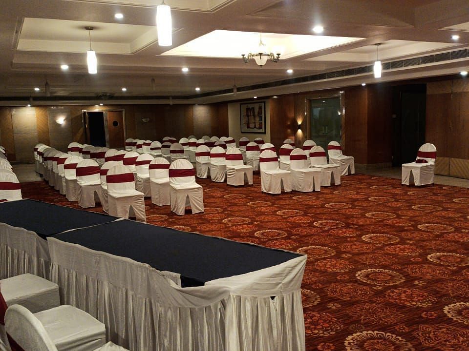 Large banquet hall with rows of chairs arranged, a carpeted floor, and lights on the ceiling, set up for a meeting or event - Lords Plaza Ankleshwar