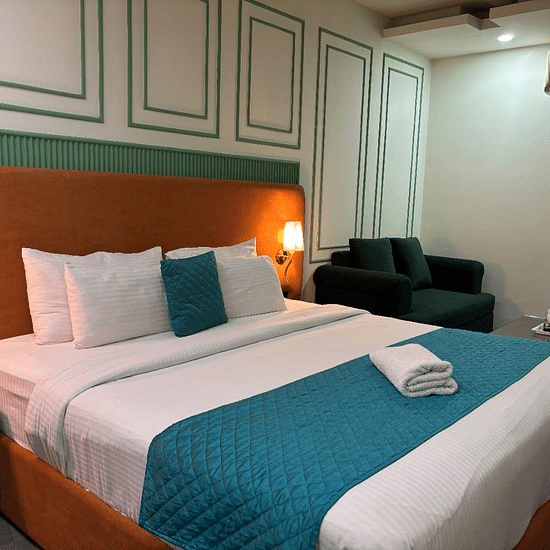 An interior view of a hotel room featuring a bed with pillows,  a sofa and decorative wall paneling - Asian Suites IFFCO Chowk Metro Station, Gurgaon. 