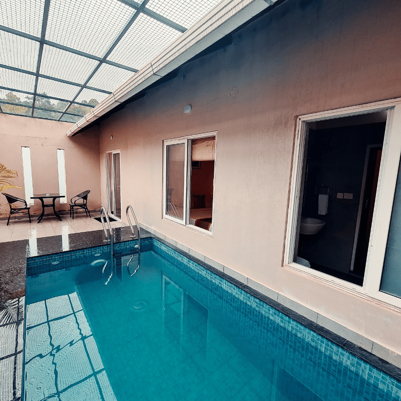 An indoor pool with a glass roof is adjacent to a building exterior, offering a bright and modern space. - Abad Brookside Lakkidi, Wayanad