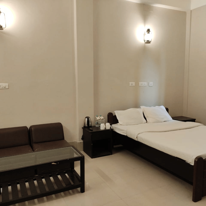 A room at Lake Side Resort Neermahal, fetauring a bed, spreads, pillows, a sofa, a table, and a window covered in curtains.