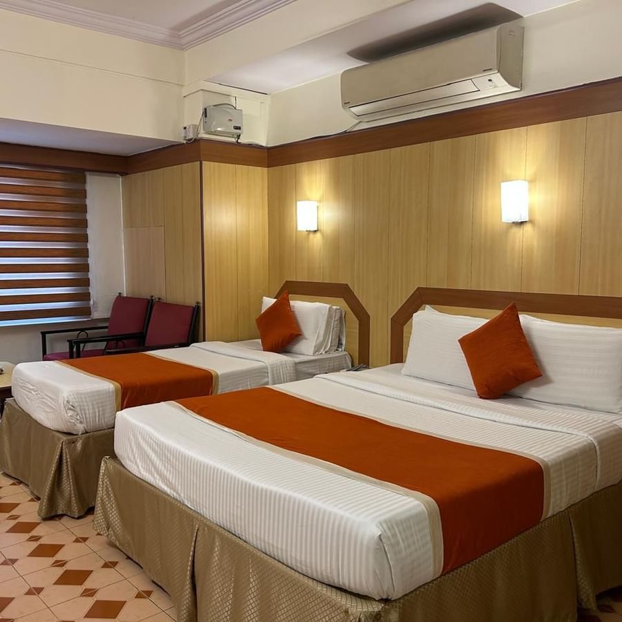 Guest room at Hotel Swagath, Bangalore featuring a double bed with white linens, orange runner, and modern wooden interiors.