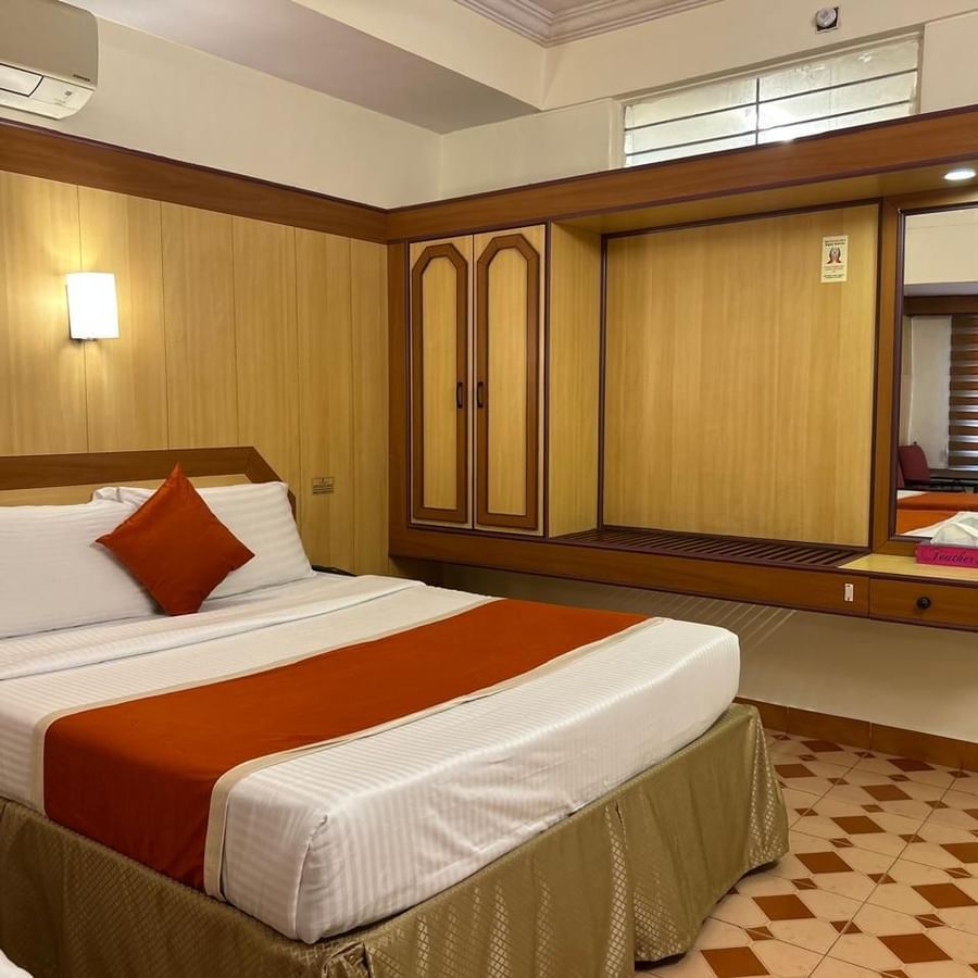 Single occupancy room at Hotel Swagath, Bangalore with a cozy bed, wooden wardrobe, and bedside lamp.