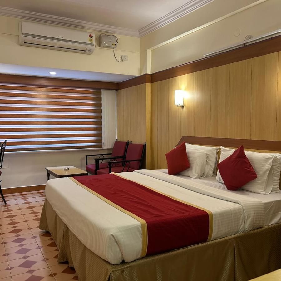 Spacious guest room at Hotel Swagath, Bangalore with two twin beds, cushioned headboards, and warm lighting.
