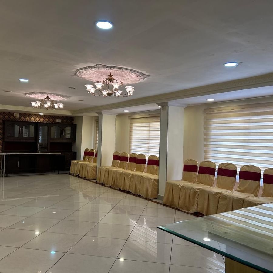 Banquet hall at Hotel Swagath, Bangalore with rows of red chairs, glossy flooring, and elegant ceiling lights.