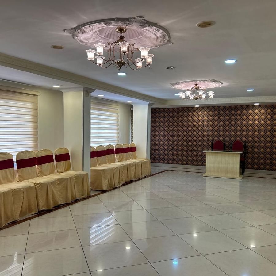 Banquet hall at Hotel Swagath, Bangalore with stage, chandelier ceiling lights, and ample seating for events.