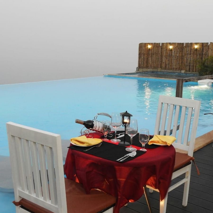 An image of a dining table by the poolside which has wine bottles and glasses placed - Polo Orchid Resort, Cherrapunji