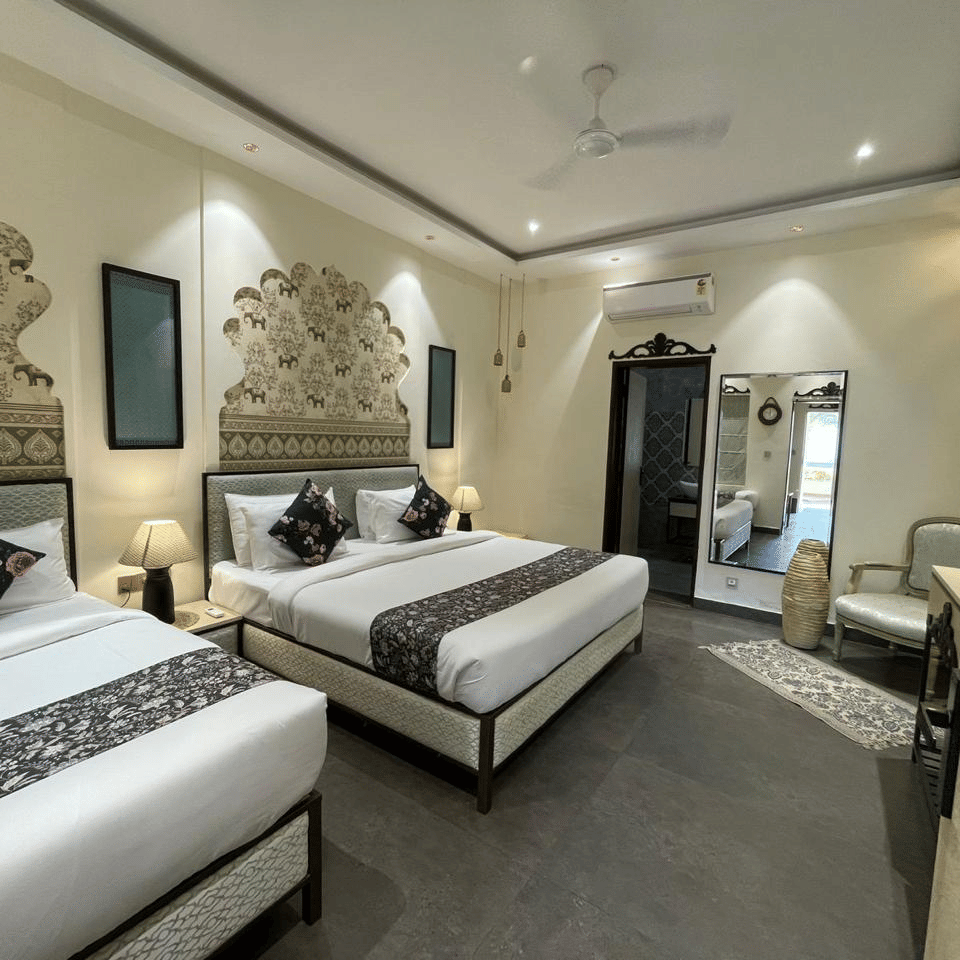 2 single beds with wall decor and lamps beside a mirror and armchair at Beelwa Palace, Jaipur