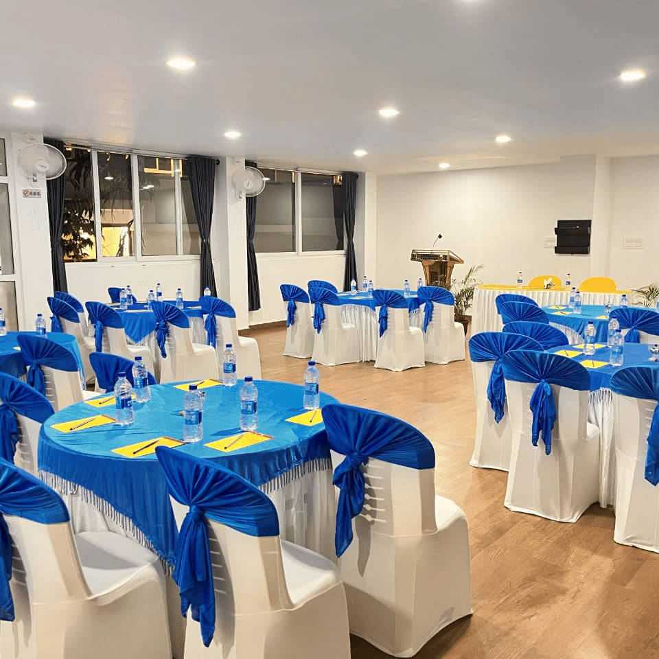 A large indoor event hall set up with many round tables and chairs, all decorated with bright blue and yellow cloth coverings at Coorg Orange Blossom Resort and Spa.