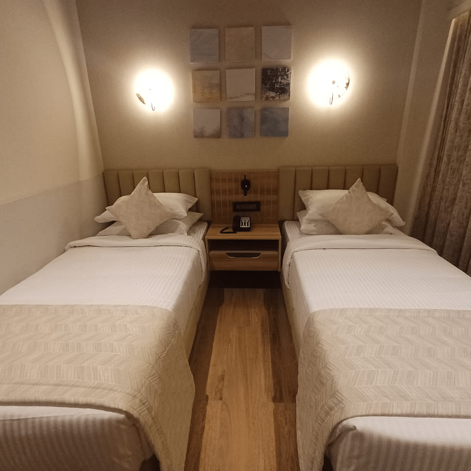 Image of a room with twin beds and a lights above the bed  at Hotel Raai, Hosur.