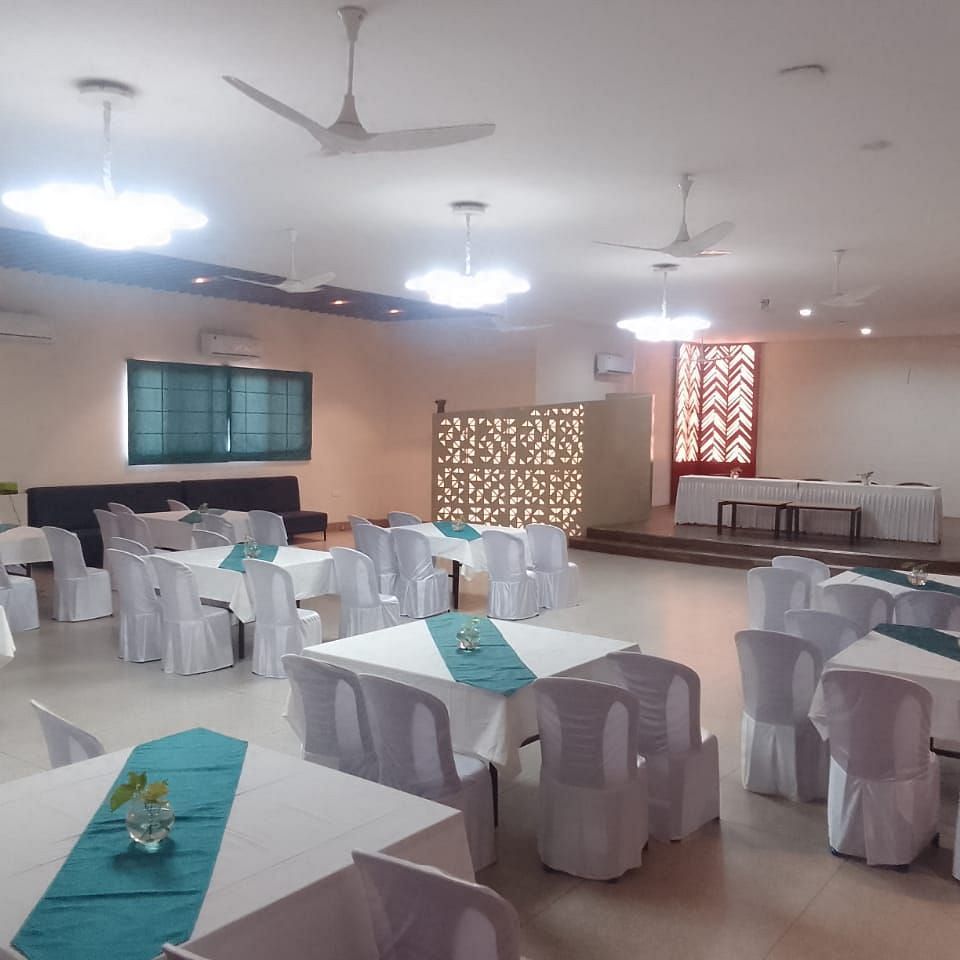 An event room with tables and chairs, a ceiling fan, and patterned curtains - Lords Eco Inn Belagavi