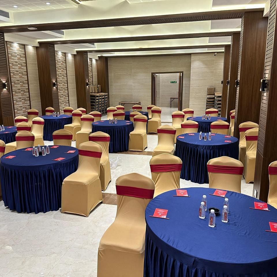 Multiple decorated seating arrangement in a spacious hall featuring round tables and chairs around it at Shyanu Lords Eco Inn Airoli.