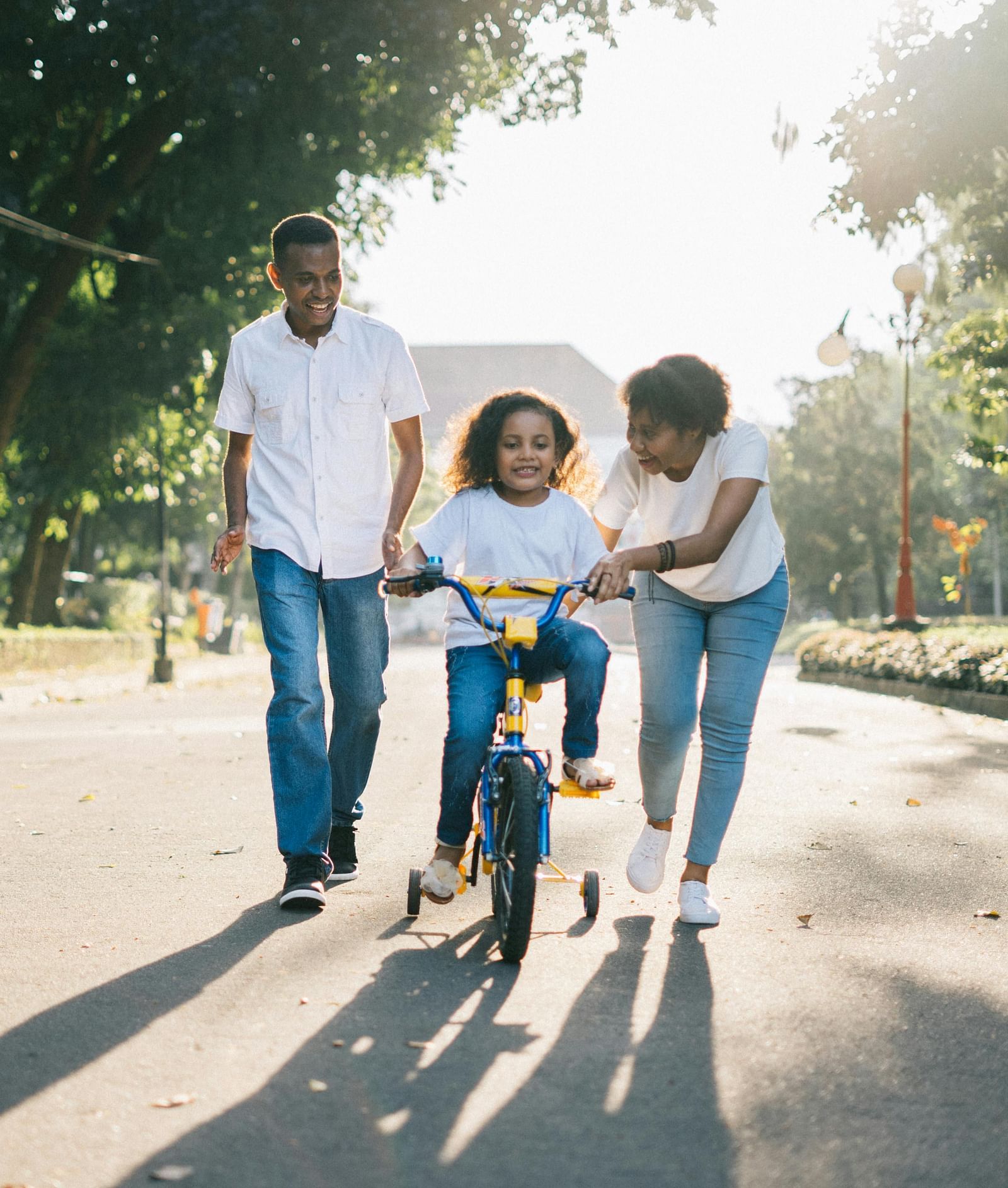 A man and woman teaching a little girl how to ride a bicycle