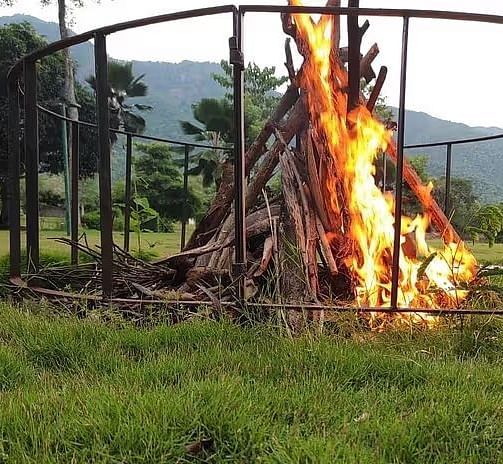A vibrant bonfire in a metal fire pit at Avana Resort, surrounded by green grass under a clear sky