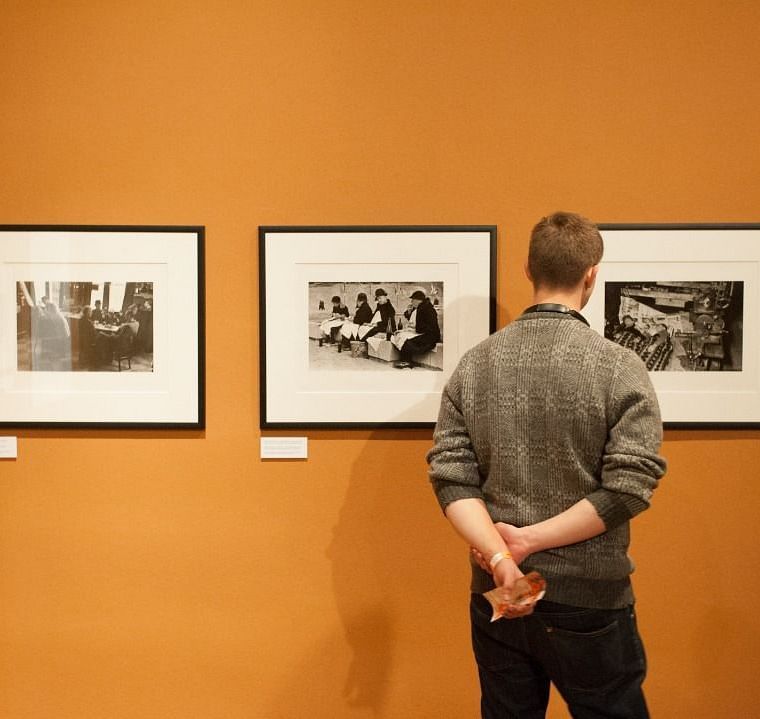  Three photographs on the wall, with one person observing them