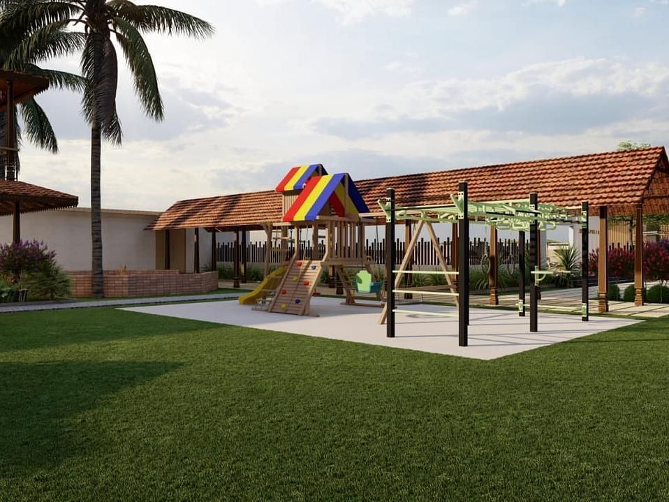 A grassy outdoor area with playground equipment and a building with a brown roof in the background, surrounded by trees and foliage.