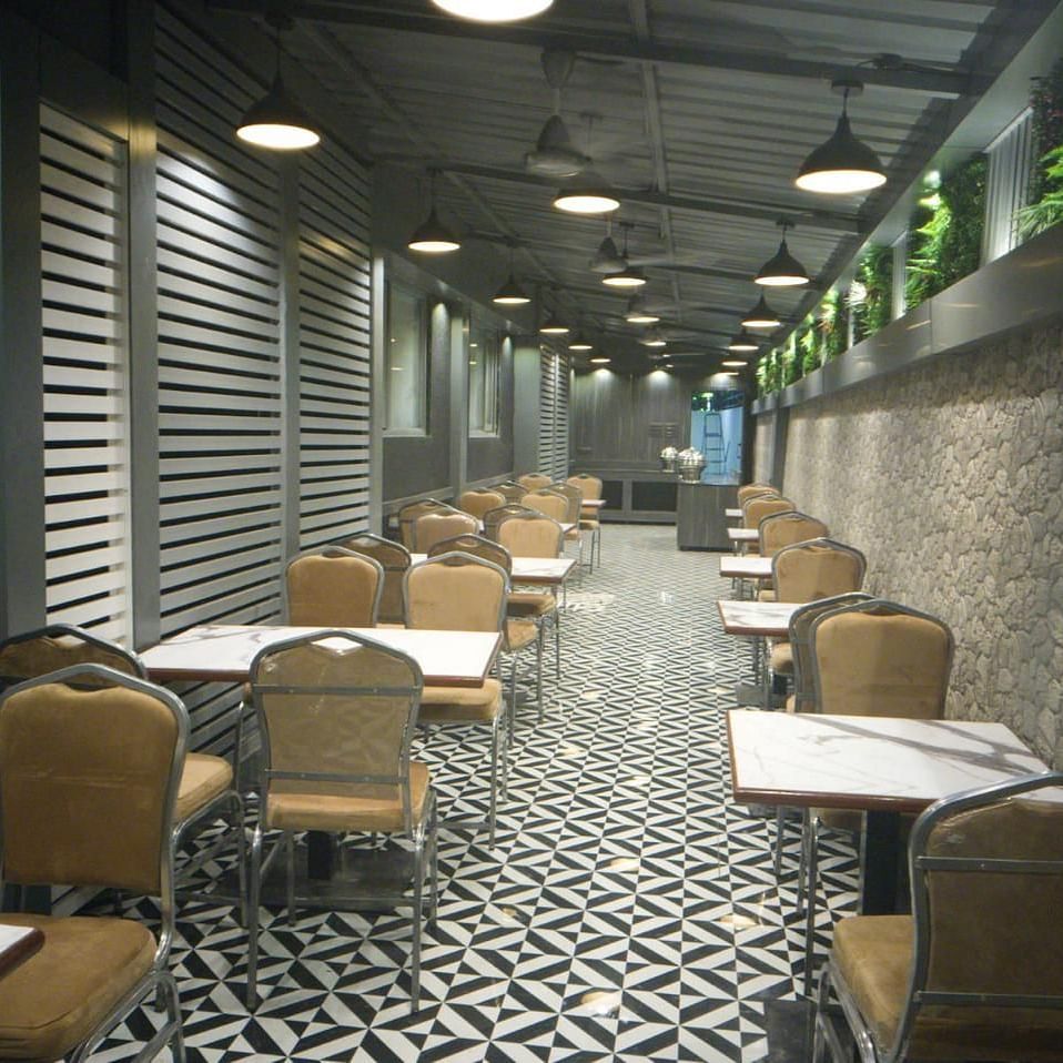 Multiple dining table set on a narrow hallway featuring patterned marble floor and pendant lights at Shyanu Lords Eco Inn Airoli.